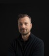 Portrait of Anders Henricson, Chief Executive Officer, at Grassfish, standing confidently with arms crossed, wearing a black sweater against a dark background.