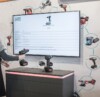 A person interacting with a smart tool display featuring a Metabo cordless drill. The digital screen above the drill provides detailed specifications and pricing information. The background includes images of various power tools connected by lines, illustrating a network of related products.
