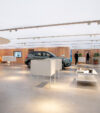 Spacious showroom with a sleek car displayed amid modern, minimalist decor. Soft lighting, wood accents, and potted plants create a calm ambiance.