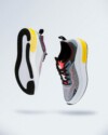 A pair of modern athletic sneakers suspended in mid-air against a light gradient background. The shoes feature a sleek design with a mix of grey, white, black, and vibrant yellow accents on the sole, along with red and blue details on the upper. The soles showcase a textured grip pattern.